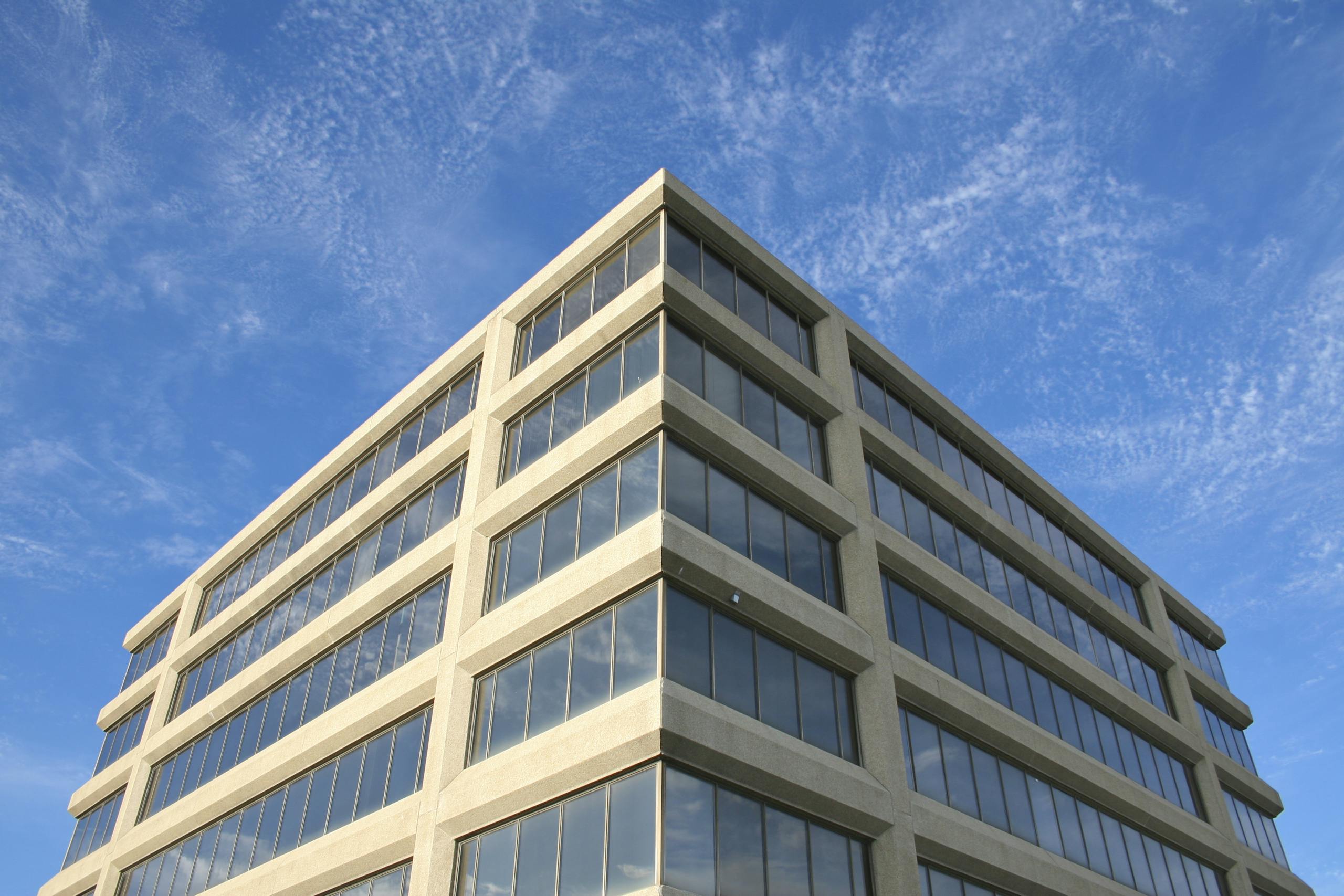 Corner view of a modern office building with reflective windows under a clear blue sky.